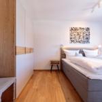 Schlafzimmer mit Bett, Nachttisch, Wandbild und Holzboden.