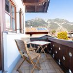 Terrasse mit Tisch und Stühlen, Blick auf Berge und Dächer.