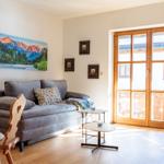 Wohnzimmer mit Sofa, Tischen und Holzboden. Große Glastür führt auf Balkon.