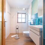 Badezimmer mit Dusche, Toilette und Waschbecken. Holzfußboden und blaue Fliesen.
