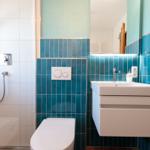 Badezimmer mit Dusche, Toilette und Waschbecken mit blauen Fliesen.