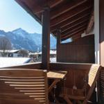 Holzterrasse mit Tisch und Stühlen, Blick auf schneebedeckte Berge und Dächer.
