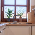 Küchenarbeitsfläche mit Fenster, Pflanzen und Wasserhahn.