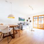 Essbereich mit Tisch und Stühlen, Sofa und Holztüren zum Balkon.