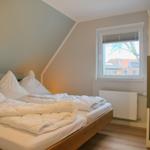 Schlafzimmer mit Dachschrägen, Bett und Fenster mit Blick auf Dächer.