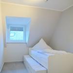 Schlafzimmer mit Dachschrägen, weißem Bett und Fenster mit Blick auf Dach.