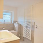 Badezimmer mit Waschbecken, Toilette und Heizkörper. Fenster mit Blick auf Dach.