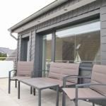 Terrasse mit Sitzgruppe und Glasgeländer. Modernes Haus mit großen Fenstern.