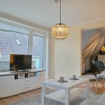 Wohnzimmer mit TV, Couch und Tisch. Küche im Hintergrund sichtbar.