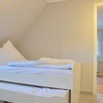 Schlafzimmer mit weißem Bett und Schiebetüren unter Dachschrägen.