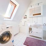 Badezimmer mit Waschmaschine, Waschtisch und Dusche unter Dachschrägen.