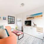 Ein Wohnzimmer mit orangefarbenem Sofa, TV-Schrank und Strandmotiven an der Wand.