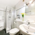 Badezimmer mit Dusche, Waschbecken und Toilette. Weiße Fliesen und gelbe Tulpen.