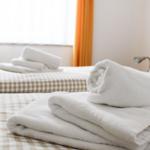 Zwei Betten mit karierten Bettwäschen und gefalteten weißen Handtüchern.