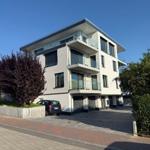 Moderne Mehrfamilienhaus mit Balkonen und gepflastertem Vorplatz.