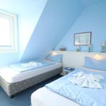 Zwei Betten in einem hellblauen Dachzimmer mit Fenster und dekorativen Gegenständen.