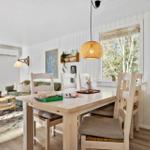 Essbereich mit Tisch und Stühlen. Im Hintergrund Wohnbereich mit Sofa und Fenstern.
