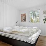Schlafzimmer mit weißem Bett, Fensterblick auf Wald und Wanddekoration.