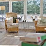 Wohnzimmer mit zwei Sesseln, Kamin und Blick auf Wald.