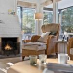 Wohnzimmer mit Kamin, Sessel und Tisch. Große Fenster mit Blick auf Wald.