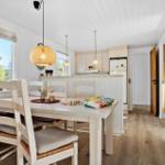 Essbereich mit Tisch, Stühlen und Blick auf Wald. Küche mit Kühlschrank und Holzboden.