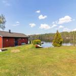 Rotes Holzhaus am See mit Boot und Grasfläche.