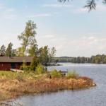 Rotes Holzhaus am Seeufer mit Blick auf Wald und Wasser.