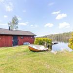 Rotes Holzhaus am See mit Boot und Grillplatz.