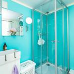 Badezimmer mit Dusche, Waschbecken und Spiegel an türkisfarbenen Wänden.