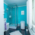 Badezimmer mit Dusche, Toilette und Waschmaschine. Blaue Wände und schwarze Fliesen.