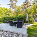 Terrasse mit Sitzgruppe, Tisch und Sonnenschirm. Hintergrund: Wald und Gartenhaus.