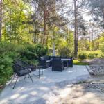 Terrasse mit Sitzgruppe und Sonnenschirm im Wald. Pflanzen und Steine umgeben den Platz.