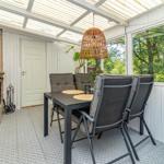 Terrasse mit Esstisch, Stühlen und Kamin. Durchgehendes Glas bietet Blick auf Grün.