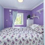 Schlafzimmer mit lila verkleideten Wänden, Fenster und Bett mit Blumenbezug.