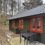 Wooden house with red window frames and outdoor terrace with table and chairs.
