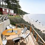 Deck with table and chairs overlooks beach and sea.