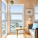 Living room with wooden walls, sofa, and ocean view through large windows.