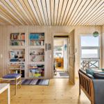 Living room with wood walls, bookshelves, and ocean view through large windows.