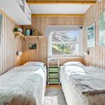 Two beds with patterned bedding, wooden walls, window, and wall shelves.
