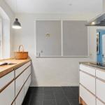 Kitchen with wooden countertop, white cabinets, and window. A board hangs on the wall.