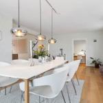 Dining area with white table and chairs, three pendant lights, and hardwood floor.