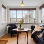 A living room with two dark armchairs, a wooden table, and large windows.