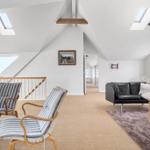 Living space with two chairs, sofa and table under sloped ceilings with skylights.