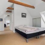 Bedroom with sloped ceiling, wooden beams, and skylight. Black bed, sliding doors, and carpeted floor.
