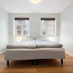 A bedroom with a double bed, two windows, and hardwood floors.