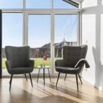 Two gray chairs sit before large windows overlooking a garden.