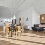 Large living and dining area with wooden floor and wood panel. Dining table with chairs and sofa.