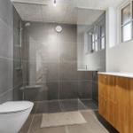 Badezimmer mit Dusche, Toilette und Waschbecken mit Holzfront