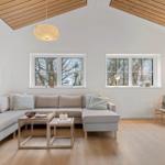 Wohnzimmer mit Sofa, Tischen und Fenstern. Holzdecke und helle Wände.