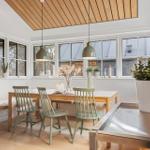 Esszimmer mit Holztisch, grünen Stühlen und großen Fenstern. Decke aus Holzdielen.
